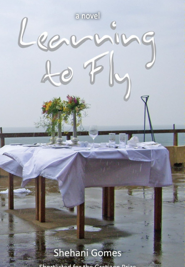 Cover of "Learning to Fly" by Shehani Gomes, featuring a decorated table beside the ocean on a rainy day.